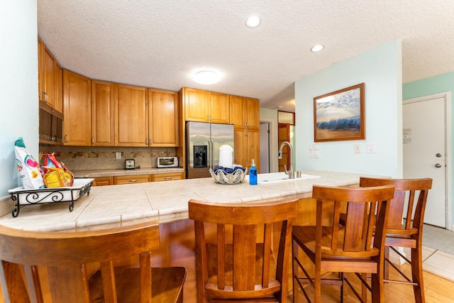 kitchen featuring kitchen peninsula, stainless steel refrigerator with ice dispenser, a breakfast bar, and tile counters