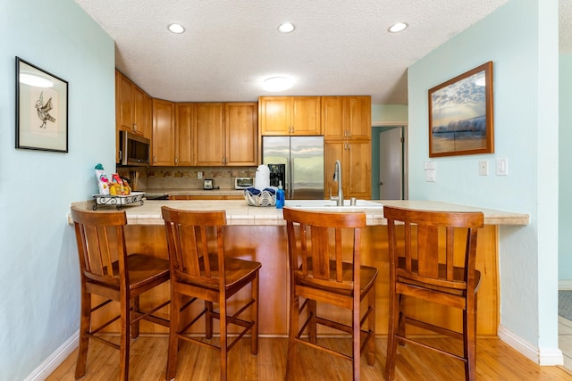 kitchen with kitchen peninsula, a kitchen breakfast bar, light wood-type flooring, stainless steel appliances, and sink