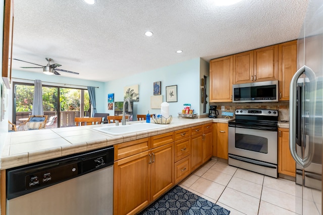 kitchen featuring sink, light tile patterned floors, tile counters, kitchen peninsula, and stainless steel appliances