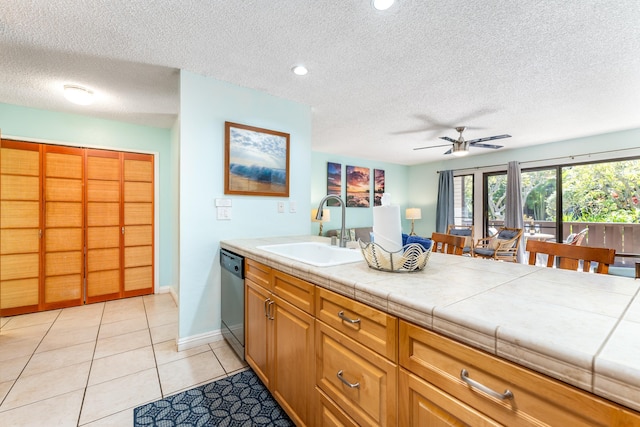 kitchen featuring ceiling fan, dishwasher, sink, tile counters, and light tile patterned floors