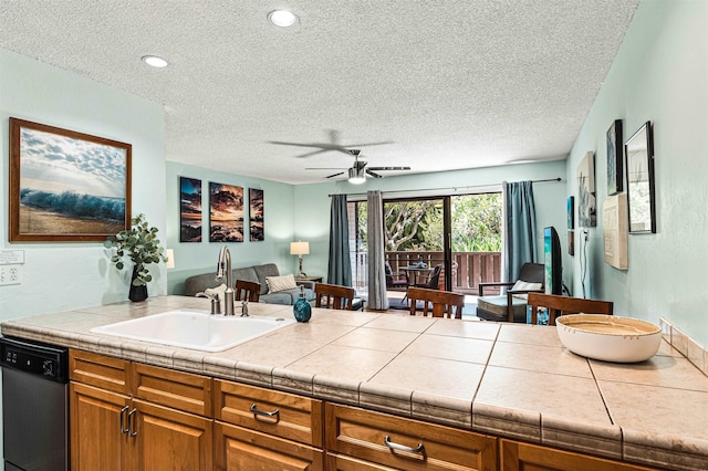 kitchen featuring sink, stainless steel dishwasher, ceiling fan, a textured ceiling, and tile counters