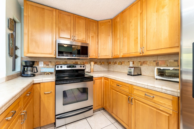 kitchen featuring tile countertops, backsplash, light tile patterned floors, a textured ceiling, and stainless steel appliances