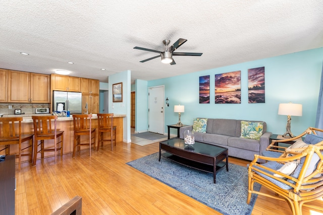 living room with ceiling fan, a textured ceiling, and light wood-type flooring