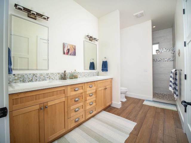 bathroom with wood-type flooring, decorative backsplash, vanity, tiled shower, and toilet