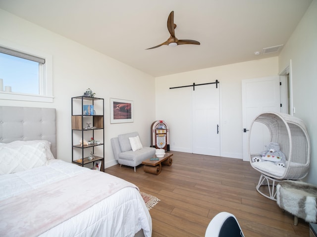 bedroom featuring dark wood-type flooring, a barn door, and ceiling fan