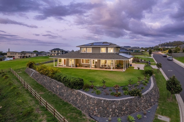 back house at dusk featuring a patio, a lawn, and solar panels