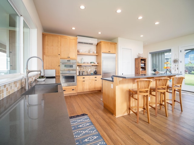 kitchen featuring backsplash, stainless steel appliances, light brown cabinetry, an AC wall unit, and light wood-type flooring