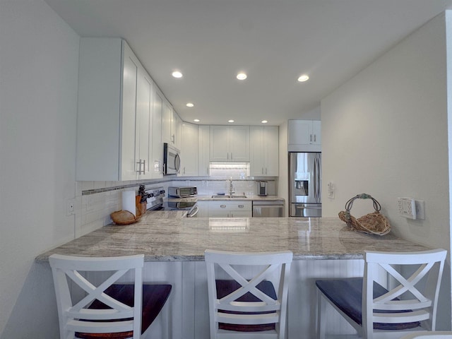 kitchen with decorative backsplash, a peninsula, white cabinetry, a sink, and stainless steel appliances