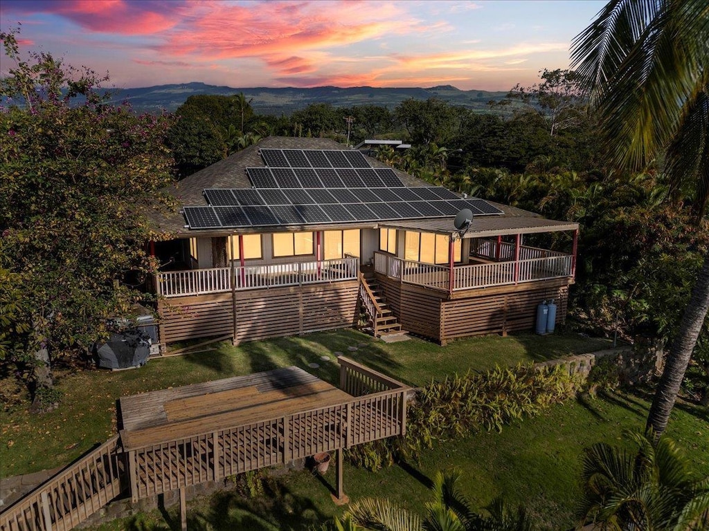 back of property with solar panels, stairway, a deck with mountain view, and a lawn