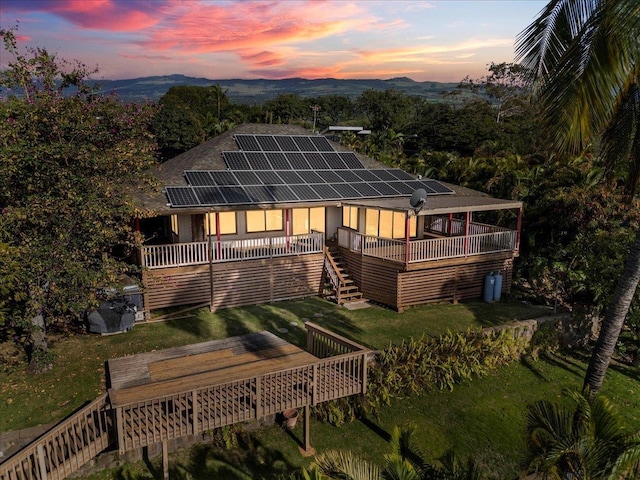 back of property with solar panels, stairway, a deck with mountain view, and a lawn