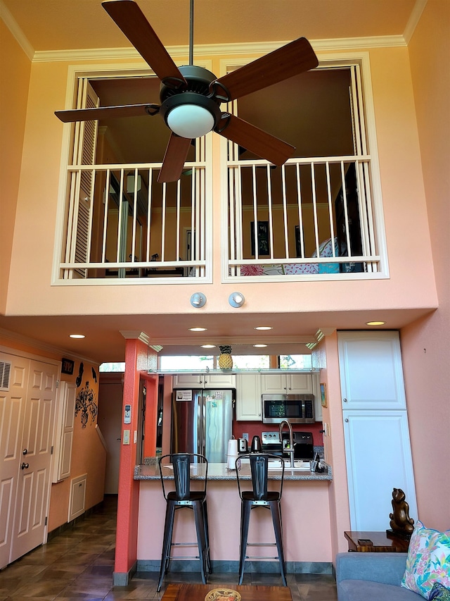 kitchen with appliances with stainless steel finishes, a breakfast bar, ceiling fan, crown molding, and sink