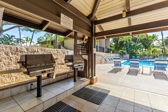 view of patio with grilling area, a community pool, and an outdoor kitchen