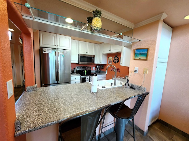 kitchen featuring white cabinets, a breakfast bar area, ornamental molding, kitchen peninsula, and stainless steel appliances