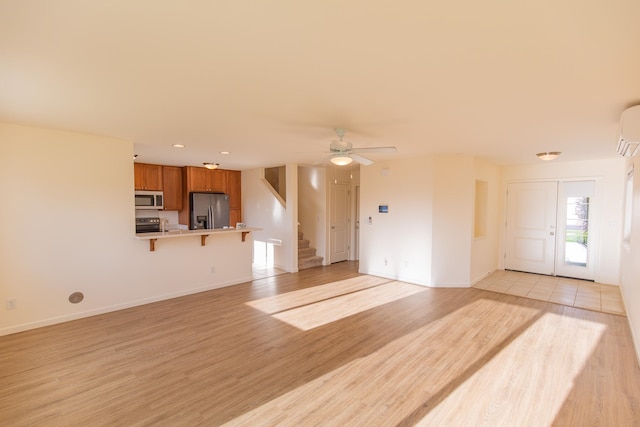 unfurnished living room featuring light hardwood / wood-style flooring, a wall unit AC, and ceiling fan