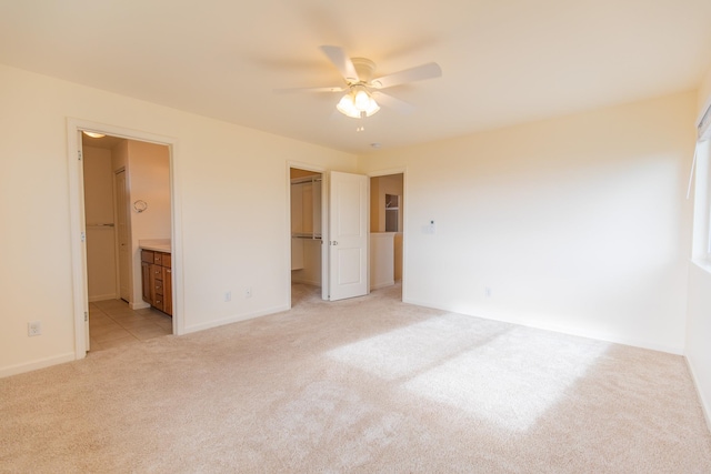 unfurnished bedroom featuring a closet, ceiling fan, a walk in closet, ensuite bath, and light colored carpet