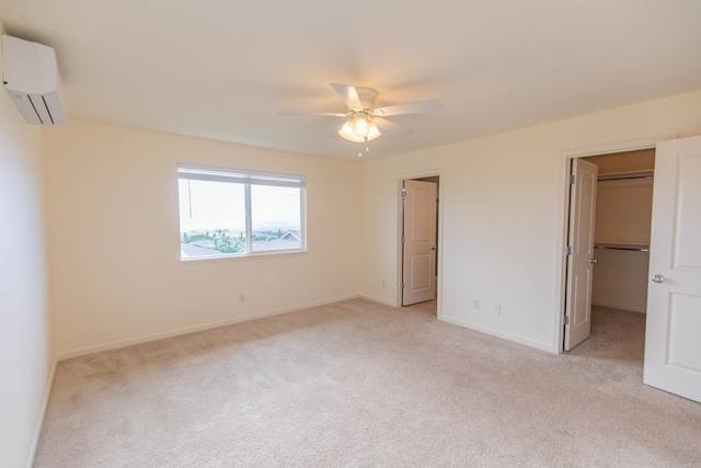 unfurnished bedroom featuring an AC wall unit, light carpet, ceiling fan, and a walk in closet