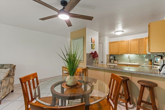 kitchen with kitchen peninsula, ceiling fan, tasteful backsplash, sink, and light tile floors