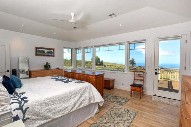 bedroom with lofted ceiling, access to outside, light hardwood / wood-style floors, a raised ceiling, and a water view