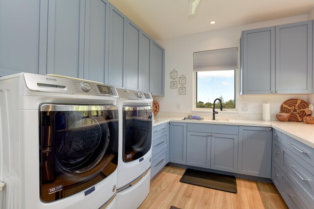 laundry room with cabinets, sink, washer and dryer, and light hardwood / wood-style flooring