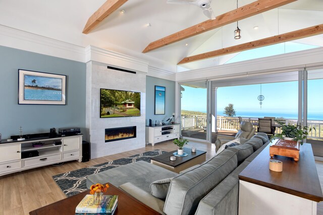 living room with a tiled fireplace, vaulted ceiling with beams, crown molding, and light wood-type flooring