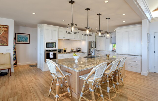 kitchen featuring white cabinetry, stainless steel appliances, hanging light fixtures, and a large island with sink