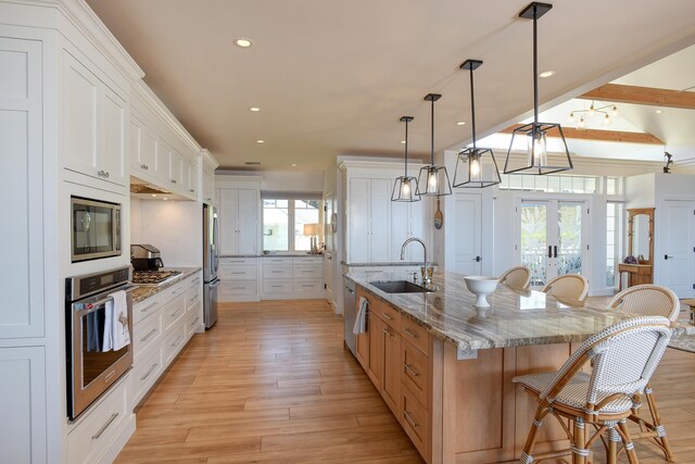 kitchen featuring appliances with stainless steel finishes, white cabinetry, hanging light fixtures, light stone counters, and a spacious island