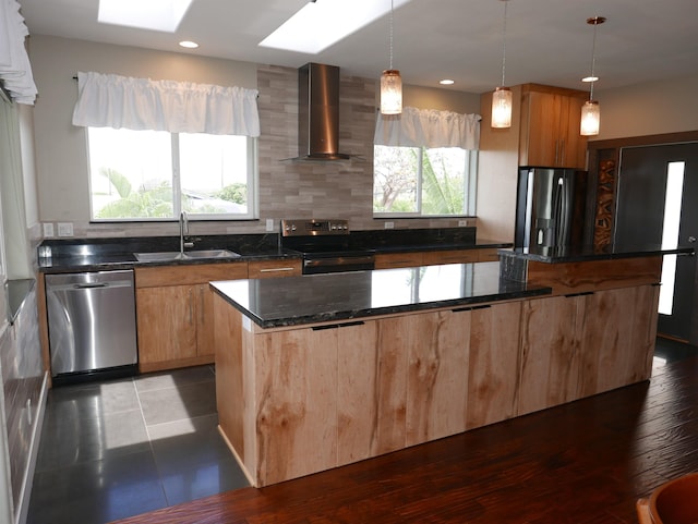 kitchen featuring wall chimney range hood, sink, dark stone countertops, appliances with stainless steel finishes, and decorative light fixtures