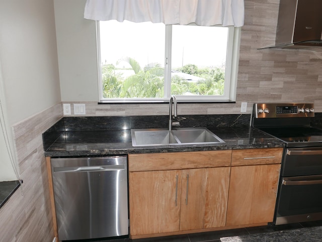 kitchen featuring sink, wall chimney exhaust hood, dark stone counters, and appliances with stainless steel finishes