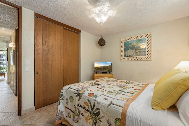 bedroom featuring ceiling fan, light tile patterned floors, a closet, and a textured ceiling