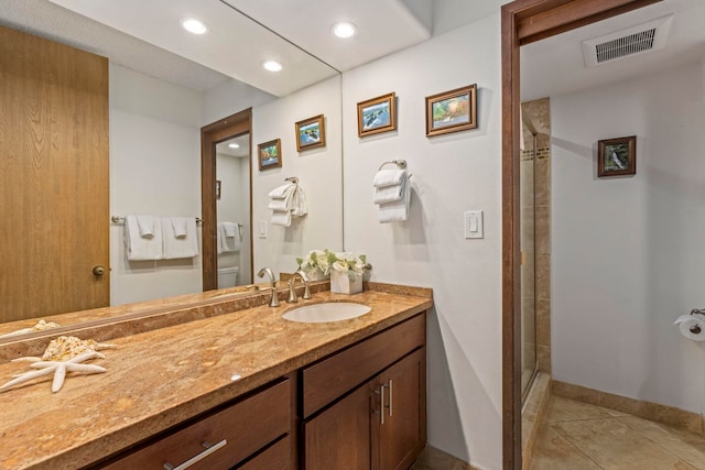 bathroom with a shower with door, vanity, tile patterned flooring, and toilet