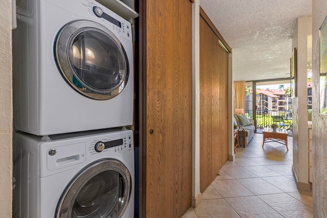 laundry area with stacked washer / drying machine, light tile patterned floors, and a textured ceiling