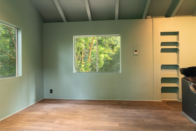 spare room with light hardwood / wood-style floors, a healthy amount of sunlight, and lofted ceiling with beams