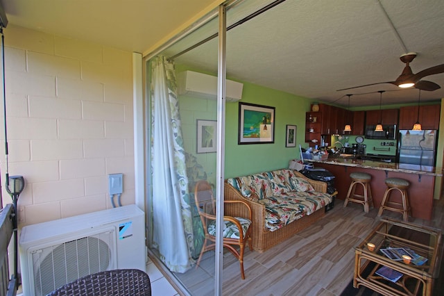 interior space featuring ceiling fan, a wall mounted AC, a textured ceiling, and light hardwood / wood-style floors