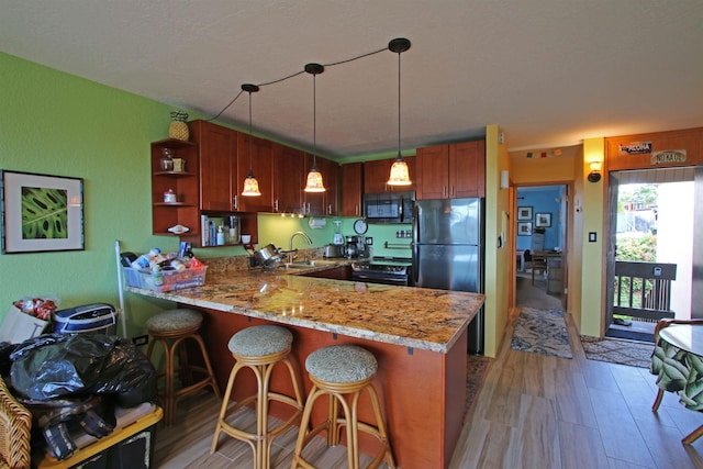 kitchen featuring decorative light fixtures, light hardwood / wood-style floors, black appliances, kitchen peninsula, and sink