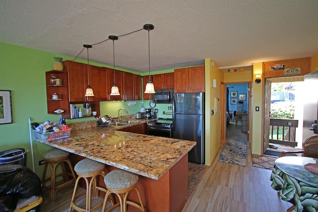 kitchen with sink, hanging light fixtures, kitchen peninsula, refrigerator, and light wood-type flooring