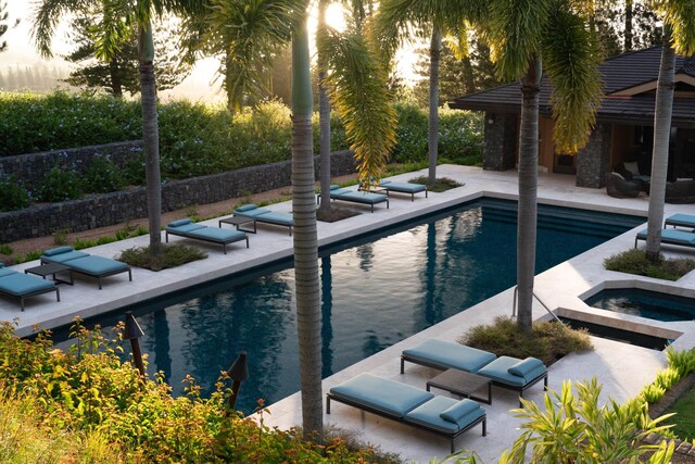 pool at dusk with an in ground hot tub, a patio area, and outdoor lounge area