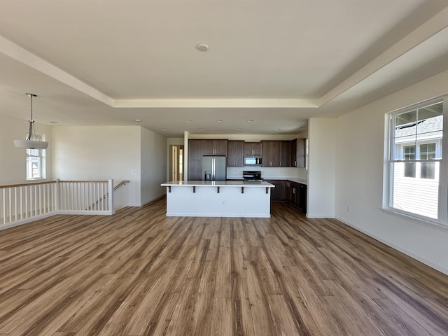 kitchen featuring appliances with stainless steel finishes, a breakfast bar, dark brown cabinets, hardwood / wood-style flooring, and a kitchen island