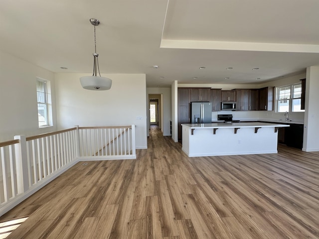 kitchen with stainless steel appliances, a kitchen breakfast bar, light hardwood / wood-style flooring, decorative light fixtures, and dark brown cabinets