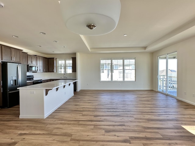 kitchen featuring sink, stainless steel appliances, a tray ceiling, a breakfast bar, and light wood-type flooring