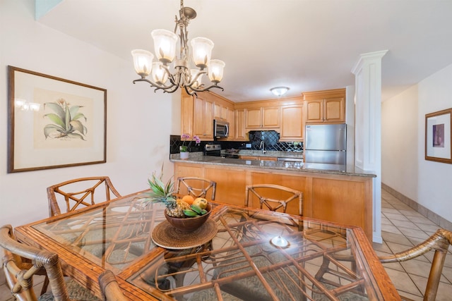 kitchen featuring stainless steel appliances, backsplash, light tile patterned flooring, a peninsula, and a notable chandelier