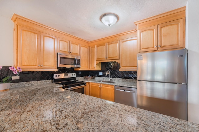 kitchen with light stone counters, stainless steel appliances, light brown cabinetry, and a sink