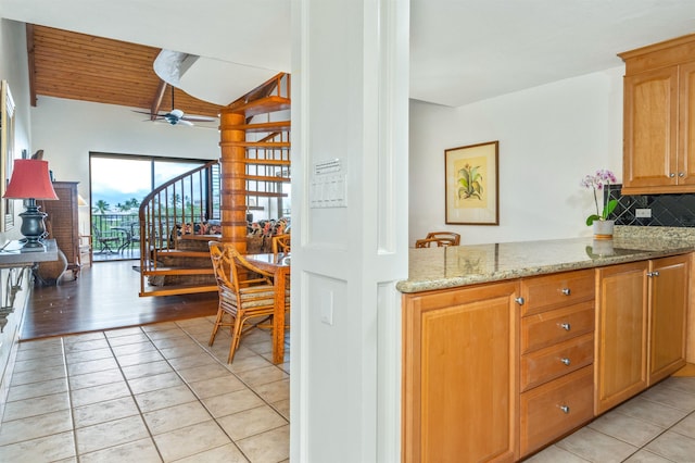 kitchen featuring a ceiling fan, light stone counters, backsplash, and light tile patterned floors