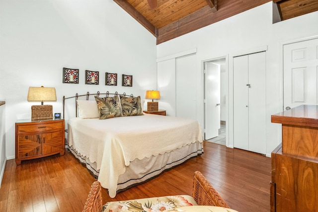 bedroom with wooden ceiling, wood-type flooring, beam ceiling, two closets, and high vaulted ceiling