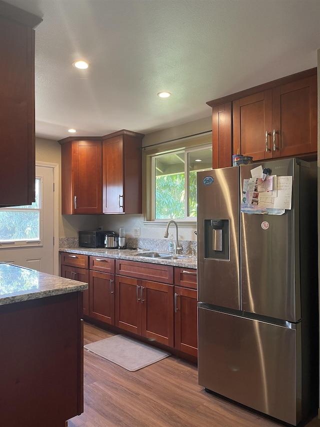 kitchen with sink, stainless steel fridge with ice dispenser, light stone counters, light hardwood / wood-style floors, and a textured ceiling