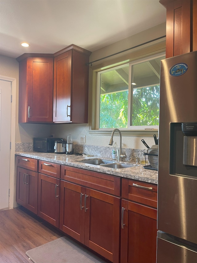 kitchen with light stone counters, sink, stainless steel refrigerator with ice dispenser, and light hardwood / wood-style flooring