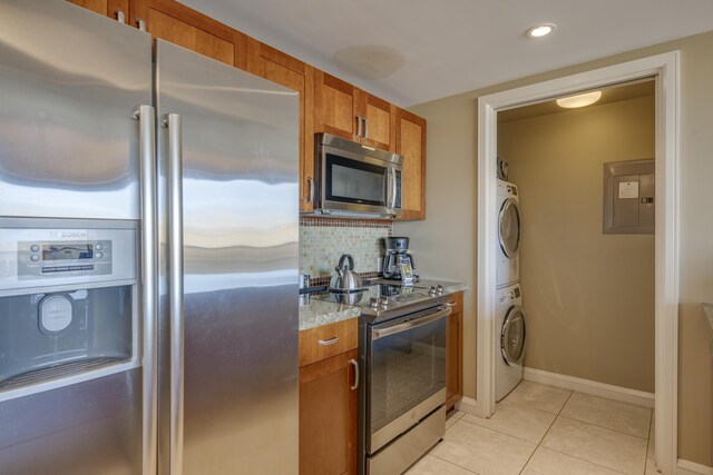 kitchen with appliances with stainless steel finishes, electric panel, light tile patterned floors, light stone countertops, and stacked washer and dryer