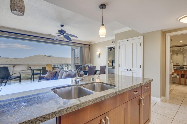 kitchen featuring light stone countertops, light tile patterned floors, sink, decorative light fixtures, and ceiling fan