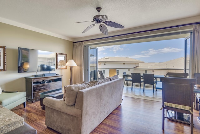 living room featuring dark wood-type flooring, a textured ceiling, ceiling fan, and ornamental molding