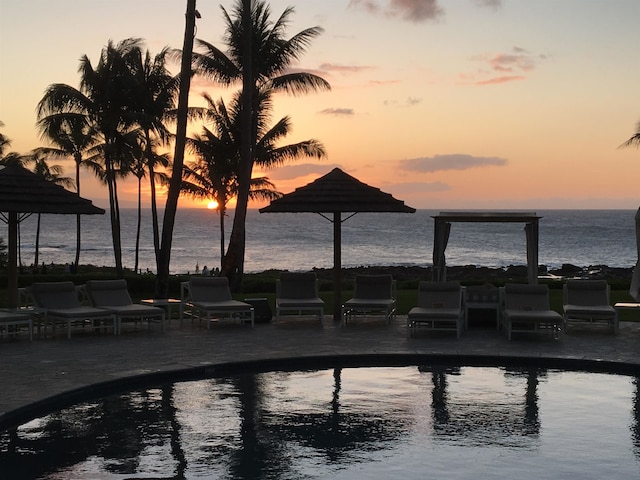 pool at dusk featuring a patio and a water view