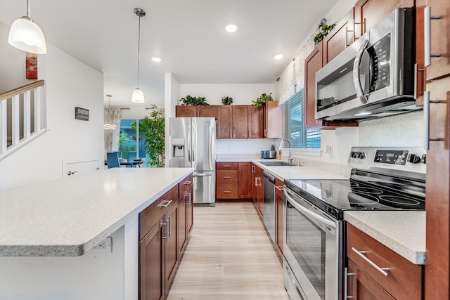 kitchen featuring appliances with stainless steel finishes, pendant lighting, sink, a center island, and light hardwood / wood-style floors